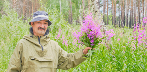 Senior man in mosquito suit holds bouquet of fireweed in his hand Chamaenerion angustifolium, Ivan tea