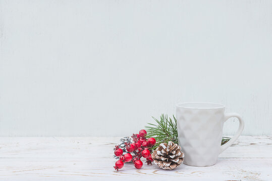 Christmas and winter template. White modern mug and christmas decorations, holly berries on white paint wooden background. Space for text