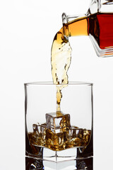 Whiskey cognac or brandy is poured from a transparent bottle into a glass cut glass with ice,...