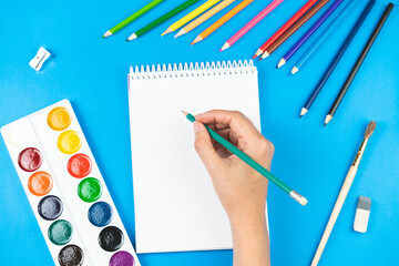 A schoolboy holds a pencil over a notepad on a blue background and supplies.