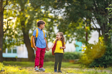 Primary school pupil. boy and a girl with backpacks are walking down the street.