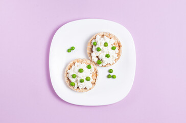 Crispbreads with cottage cheese and green peas on a pink background