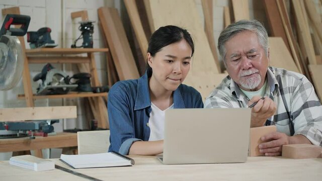 Asian senior man and women carpenter working in wood shed and designs furniture parts with laptop computer at home.  Asian carpenter has creativity the component wood parts at home.