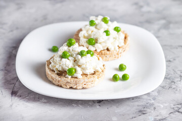 Crispbreads with cottage cheese and green peas on a white plate