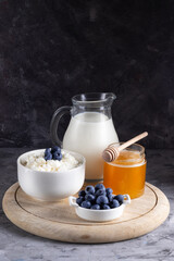 Grain cottage cheese in a white plate with blueberries with sour cream, milk and honey on a wooden stand