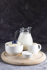 Grain cottage cheese in a white plate with sour cream, cream and milk on a wooden stand