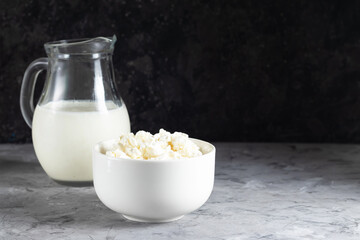 Grain cottage cheese in a white plate with jugs of milk on a dark background