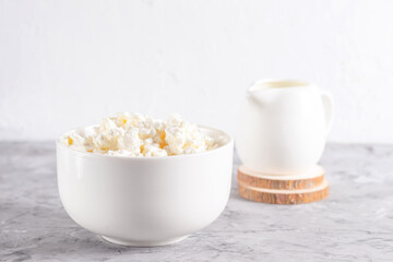 Grain cottage cheese in a white plate with a cream milk jug on a light background