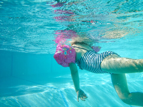 Litle girl swimmng in a pool dress in a stripes swim suit