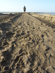 hombre andando por camino de arena con agua a los lados