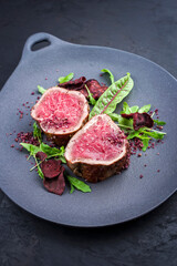 Gebratene dry aged Angus Filet Medaillon Steaks natural vom Rind mit Gemüse Chips und Salat angeboten als close-up auf einem Modern Design Teller