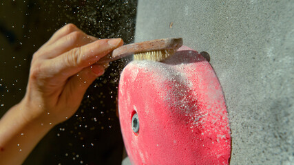 MACRO: Female climber uses a brush to get rid of magnesium stuck to a pink crimp