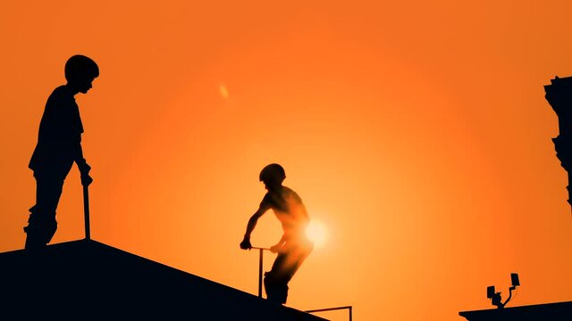 Unrecognizable teenage boy silhouette showing high jump tricks on scooter against orange sunset sky at skatepark - slow motion. Sport, extreme, freestyle, outdoor activity concept