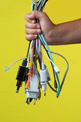 Several multi-colored wires from household appliances in hand on a yellow background.