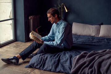 young man reading a book, a guy in a blue shirt in the interior of a stylish apartment