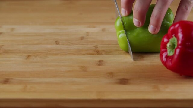 Woman's Hand Cutting Green And Red Bell Peppers Into Thin Slice On A Wooden Board Using A Chef's Knife - Closeup Shot