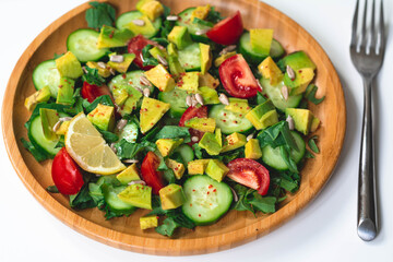 Fresh and healthy summer salad with cucumbers, tomatoes, avocado, arugula, sunflower seeds, lemons and chili flakes. Seasoned with olive oil. White background