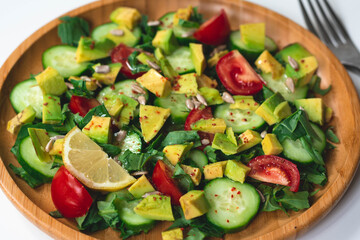 Fresh and healthy summer salad with cucumbers, tomatoes, avocado, arugula, sunflower seeds, lemons and chili flakes. Seasoned with olive oil. White background