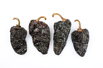 Dried Mexican black hot mulato chili offered as close-up on white background with copy space - free-form select - obrazy, fototapety, plakaty