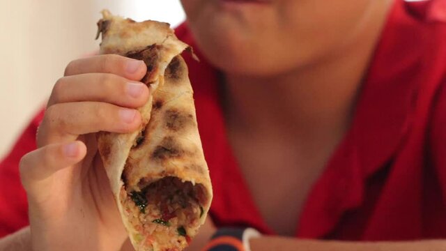 Boy hungrily bites and chews rolled Turkish pizza lahmacun. High quality FullHD footage