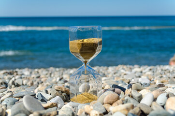 Hourglass on sea pebbles against the blue sea.