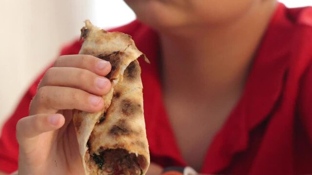 Boy hungrily bites and chews rolled Turkish pizza lahmacun. High quality FullHD footage