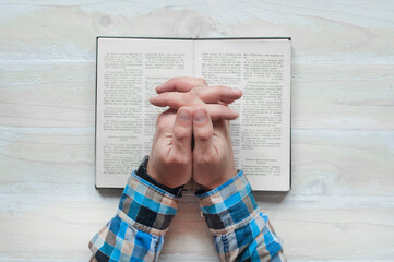 Open book Bible. Hands of a man in prayer. On a wooden background