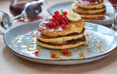 Fresh homemade pancakes with red currants and caramel on gray plate and craft background with black and strong coffee. Delicious breakfast and pastries.