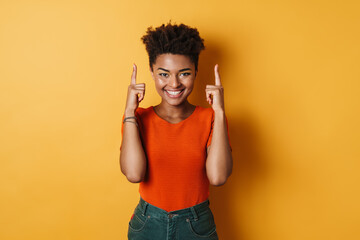 Image of african american woman pointing fingers upward and smiling