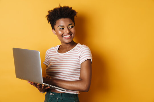 Image of joyful african american woman smiling and using laptop