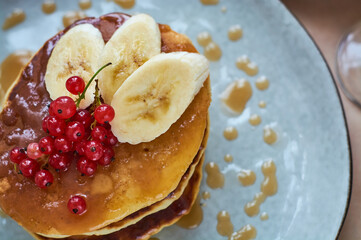 Fresh homemade pancakes with red currants and caramel on gray plate and craft background with black and strong coffee. Delicious breakfast and pastries.