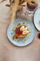 Fresh homemade pancakes with red currants and caramel on gray plate and craft background with black and strong coffee. Delicious breakfast and pastries.