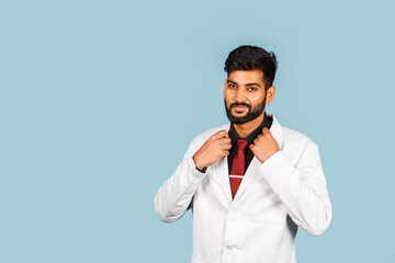 Handsome modern indian / asian doctor with stethoscope, tie and white coat on blue background