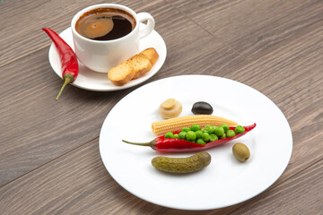 Canned vegetables salad and a cup of black coffee with red pepper and crackers on plates