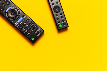 Black TV and audio remote control on bright yellow background flat lay top view copy space....