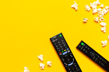 Black TV, audio remote control and popcorn on bright yellow background flat lay top view copy...