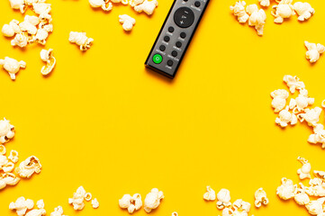 Fototapeta na wymiar Black TV remote control and popcorn on bright yellow background flat lay top view copy space. Minimalistic background with a remote control, watching a movie, series, set-top boxes, audio system