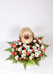 A toy dog or bear with a bouquet of different flowers