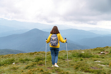 Young attractive woman with nordic walking poles hiking outdoors. Hiking and resting in mountains. Back view, full length