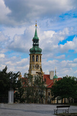 Church of the Nativity of the Lord (Prague Loreta - Pražská Loreta) in Hradcany surrounded by green trees against the background of clouds on a summer, Sunny, hot day.