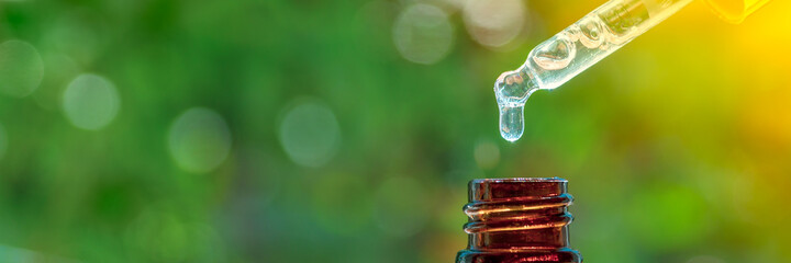 Cosmetic pipette with drops of cosmetic oil close-up on a green nature background. Essence liquid cosmetic. Perfume. Aromatherapy. Banner. Copy space.