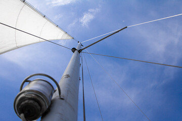 Bottom view of mast and sail of yacht on blue sky background, selective focus