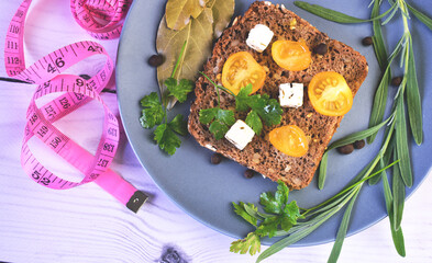 Healthy vegetarian sandwich with feta cheese, yellow cherry tomatoes and herbs on the plate. Pink centimeter tape. Tasty snack breakfast, vegan food. Brown bread sandwich. Weight loss concept.