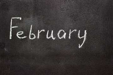 Fototapeta premium Month written in white chalk on a chalkboard. The month depicted on the chalkboard is February