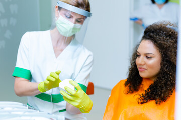Caucasian female dentist talking to mixed race teenage patient, explaining importance of oral hygiene on jaw model.