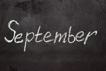 Fototapeta premium Month written in white chalk on a chalkboard. The month depicted on the chalkboard is September