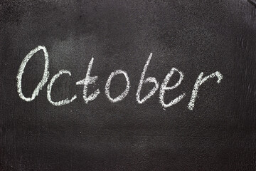 Fototapeta premium Month written in white chalk on a chalkboard. The month depicted on the chalkboard is October
