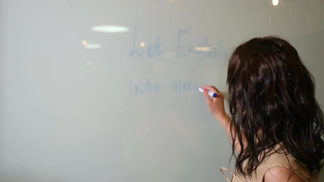 Woman write something with note on white background. Young serious female english school teacher holding marker in right hand writing text whiteboard classroom.
