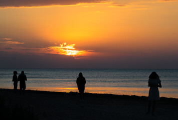 Fototapeta na wymiar Tourists at sea on the beach, admire the sunrise. Silhouettes of people
