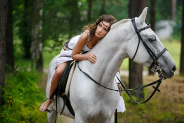 Foto op Canvas Young beautiful girl with white horse at summer green forest. Caucasian woman horseback rider in dress in boho style. Summertime scene © digitalien